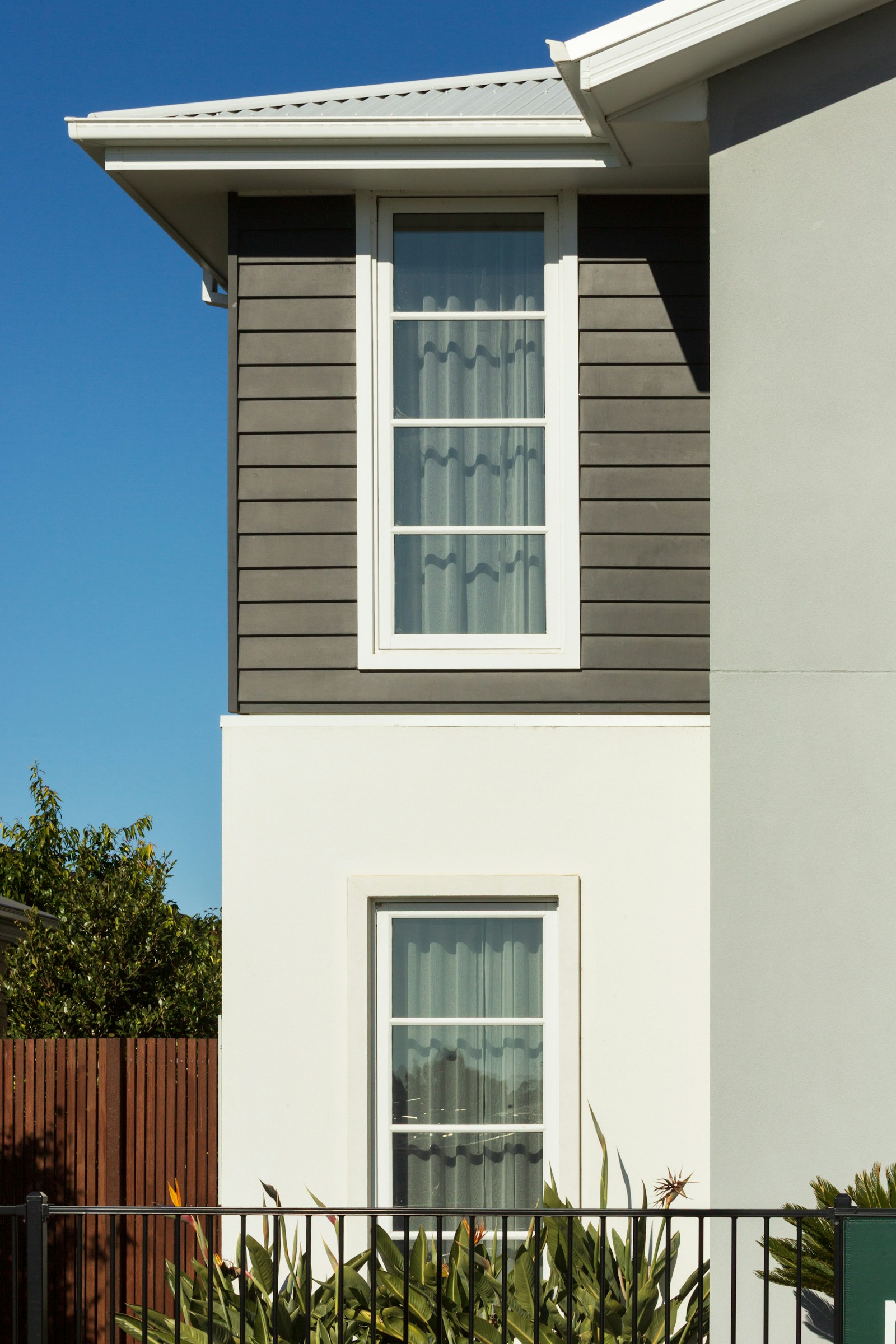 Close view of a home exterior, window, eaves, and roofline beneath a clear sky.
