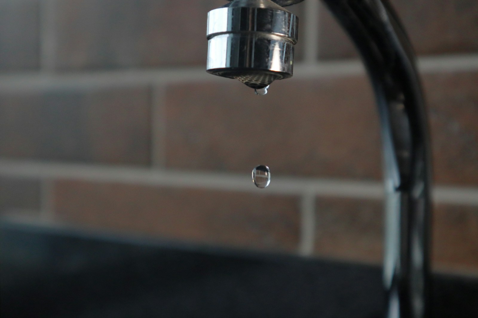 A water droplet forming below an indoor faucet.